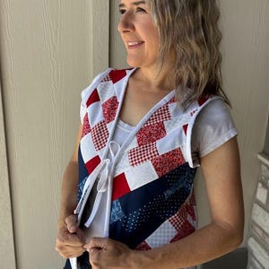 Könnte beinhalten: Eine gesteppte Weste mit patriotischem Thema. Die Weste hat ein Patchwork-Design mit roten, weißen und blauen Stoffen. Die Weste hat eine weiße Paspel und einen Kordelverschluss. Die Weste ist ärmellos und scheint handgefertigt zu sein.