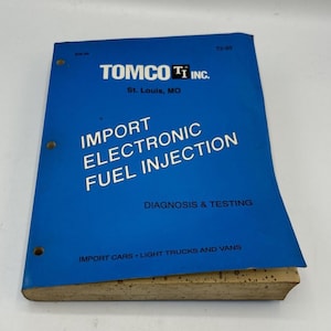 May include: A blue manual titled "IMPORT ELECTRONIC FUEL INJECTION" by TOMCO Ti Inc. The cover text includes "DIAGNOSIS & TESTING" and "IMPORT CARS • LIGHT TRUCKS AND VANS". The manual has three ring binder holes and a beige edge.