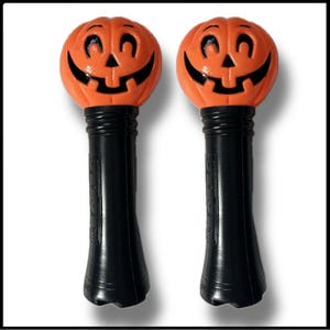 May include: Two orange plastic pumpkin-shaped Halloween noisemakers with black handles.