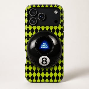 May include: A phone case with a black and neon green diamond pattern. A black Magic 8-Ball is attached to the case, displaying the text "ASK AGAIN AT MIDNIGHT" on a blue background. The number 8 is visible.