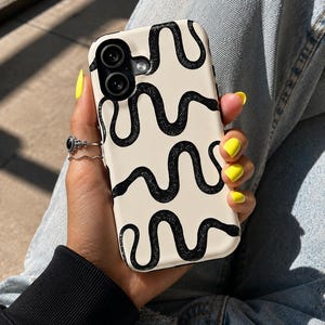 Puede incluir: Una funda para smartphone de color crema con un patrón repetitivo de líneas negras, onduladas y texturizadas que se asemejan a serpientes. La funda tiene un recorte para un sistema de cámara de doble lente en la esquina superior izquierda.