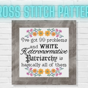 May include: Cross stitch pattern in a wooden frame. The text reads "I've got 99 problems and WHITE Heteronormative Patriarchy is basically all of them." Floral accents in pink, orange, and purple surround the text.
