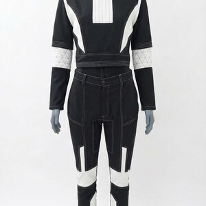 May include: A black and white two-piece outfit on a mannequin. The top is a long-sleeved crop top with white accents and a high collar. The pants are high-waisted with white panels and stitching. The outfit has a futuristic design.