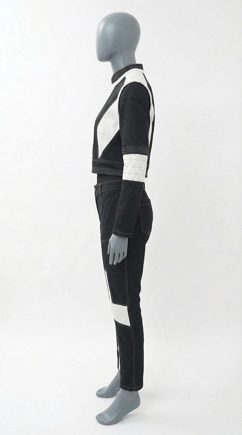 May include: A black and white two-piece outfit on a mannequin. The cropped jacket has white geometric accents and a high collar. The matching pants have white panels and stitching. The outfit is a modern, geometric design.