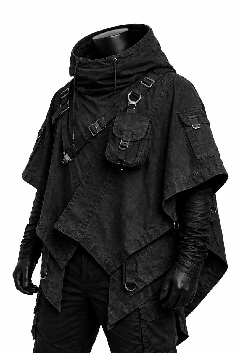 May include: A black hooded poncho featuring an asymmetrical hem, multiple utility pockets with metal buckles, and adjustable straps across the chest. The garment includes a high collar with drawstring cords and long sleeves with textured detailing.
