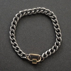 May include: A silver-toned metal curb chain bracelet featuring a polished finish. The bracelet is secured with a gold-toned rectangular carabiner-style clasp that includes a small, hexagonal screw-lock mechanism at the bottom of the link.