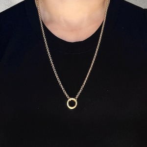 Pode incluir: Um colar dourado com uma corrente fina e um pequeno pingente circular. O colar é exibido sobre um fundo preto, destacando seu design simples. A corrente é feita de pequenas elos conectados.