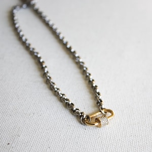 May include: A silver chain necklace with a gold clasp featuring a row of small clear stones.