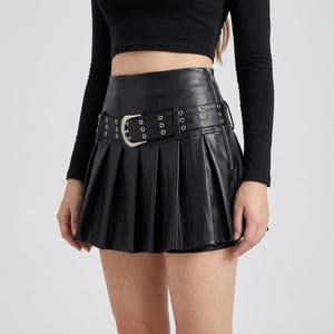 May include: A black high-waisted pleated mini skirt made of a smooth material. The skirt features a wide integrated belt with silver-toned metal eyelets and a matching silver-toned buckle. A vertical zipper is visible along the left side seam.