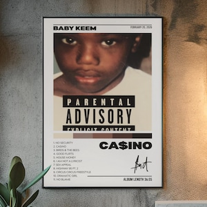 May include: A framed poster featuring Baby Keem with the text "Parental Advisory Explicit Content." The poster includes a tracklist for the album "Casino" and the artist's signature. The poster is displayed on a concrete wall.
