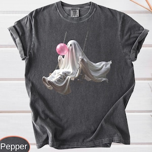 May include: A charcoal gray short-sleeve t-shirt featuring a graphic of a white ghost sitting on a swing and blowing a large pink bubblegum bubble. The shirt has a crew neckline and a washed-out, vintage-inspired fabric texture throughout.