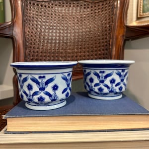 May include: Two small, round ceramic bowls featuring a white base with a repeating blue floral and vine pattern. Each bowl has a wide, flared rim and a slightly tapered base, showcasing a consistent blue and white color scheme throughout.