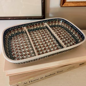 May include: A rectangular ceramic serving dish with three divided sections. The dish features a cream-colored base with a repeating pattern of small red flowers, green leaves, and dark blue vines, finished with a dark blue rim along the edges.
