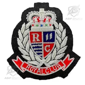 May include: A black embroidered patch featuring a silver crown above a shield divided into four quadrants with red and blue sections. The shield is surrounded by silver laurel leaves and sits above a red ribbon banner with the text ROYAL CLUB.