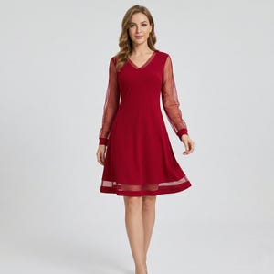 Könnte beinhalten: Ein bordeauxfarbenes Kleid mit V-Ausschnitt und transparenten, gepunkteten langen Ärmeln. Das Kleid hat einen ausgestellten Rock mit transparentem Saum. Das Model steht vor einem schlichten Hintergrund.