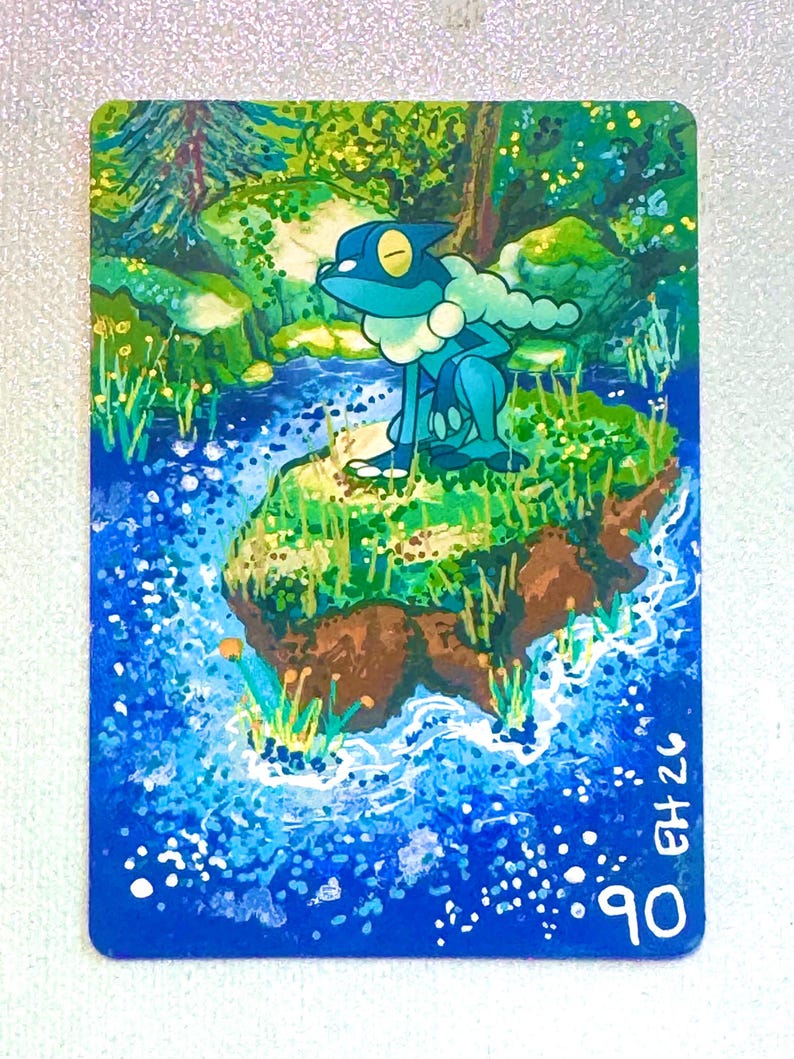 K&ouml;nnte beinhalten: Eine rechteckige Sammelkarte mit einer gemalten Illustration eines blauen, froschartigen Wesens mit wei&szlig;em Halskrausen-Detail, das auf einer grasbewachsenen Insel in einem blauen Bach sitzt. Unten rechts stehen der Text EH 26 und die Zahl 90.