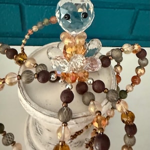 May include: A decorative octopus figurine crafted from faceted clear crystal beads for the head and a combination of amber, brown, and grey spherical beads forming the eight tentacles, featuring two small black beads as eyes on the crystal head.