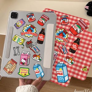 May include: A clear iPad case adorned with Hello Kitty stickers, featuring jam jars, milk cartons, and bottles. A red and white gingham pattern is visible on a separate item. The case has a white stand.