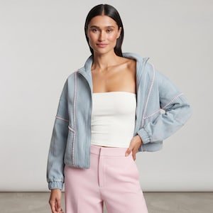 May include: A light blue zip-up jacket featuring vertical rows of small white beads along the front panels and sleeves, paired with a plain white strapless tube top and light pink high-waisted trousers with a center seam and side pockets.