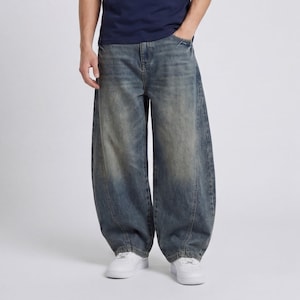 Könnte beinhalten: Verblasste blaue Jeans mit weitem, baggy Schnitt. Die Jeans haben ein klassisches Fünf-Taschen-Design und einen Knopf- und Reißverschluss. Das Model trägt weiße Turnschuhe. Die Jeans haben einen Vintage-Look.