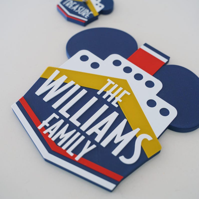 Puede incluir: Un letrero de nombre de familia con tem&aacute;tica de crucero azul y amarillo con el texto "The Williams Family" en letras blancas. El letrero tiene forma de orejas de Mickey Mouse.