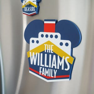 Puede incluir: Un im&aacute;n azul y amarillo con forma de Mickey Mouse con el texto "The Williams Family" sobre un fondo blanco con forma de barco. El im&aacute;n tiene una franja roja en la parte superior y una franja roja en la parte inferior.