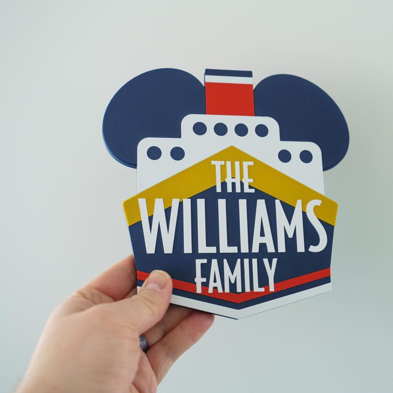 Puede incluir: Un letrero de nombre de familia de estilo n&aacute;utico azul y amarillo con un dise&ntilde;o de oreja de Mickey Mouse. El letrero dice "The Williams Family".