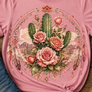 May include: A dusty pink short-sleeve t-shirt featuring a circular graphic print. The design displays a central arrangement of green cacti and pink roses, surrounded by a decorative border of feathers, geometric shapes, and a desert landscape.