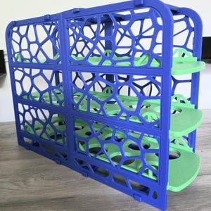 May include: A blue and green 3D-printed storage rack. The rack features a geometric design with openwork sides and three green shelves. The structure is made of a vibrant blue plastic, with the shelves in a contrasting green color.