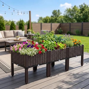 Può includere: Un'aiuola rialzata marrone piena di fiori e verdure colorate. L'aiuola ha un design intrecciato ed è sostenuta da gambe marroni scure. Il giardino è all'aperto su un ponte di legno, con un'area salotto sullo sfondo.