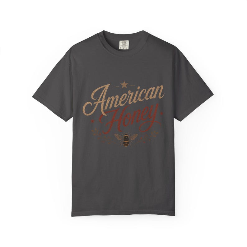 May include: Charcoal grey t-shirt featuring the text "American Honey" in a retro design. The words are in tan and red, with a star and bee illustration. A comfortable tee for casual wear.