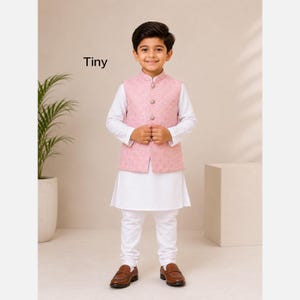 Puede incluir: Un niño viste un kurta blanco de manga larga y pantalones blancos a juego, junto con un chaleco rosa claro sin mangas con textura acolchada, cuello mao y cuatro botones redondos en la parte delantera. La palabra Tiny está impresa en negro.