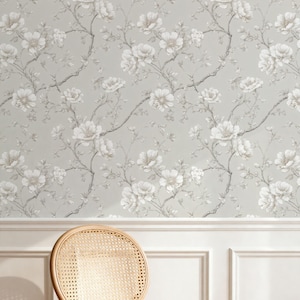 May include: Wallpaper with a floral design of white flowers and grey branches on a pale grey backdrop. A woven chair is in the foreground, with white paneling below the wallpaper.