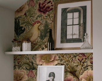 May include: A shelf with decorative items against a floral wallpaper background. Items include framed art, a dark glass bottle, a clear glass bottle, and small jars. The wallpaper features large pink and yellow flowers and a bird.