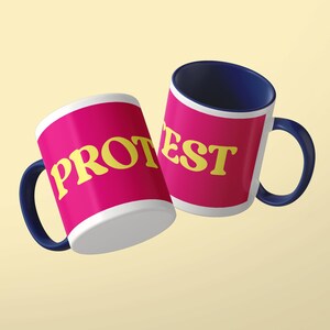 May include: Two ceramic mugs with dark blue handles and interiors. The exterior of each mug features a bright pink background with the yellow text PROTEST printed in a bold, serif font. The mugs are positioned at an angle against a light background.