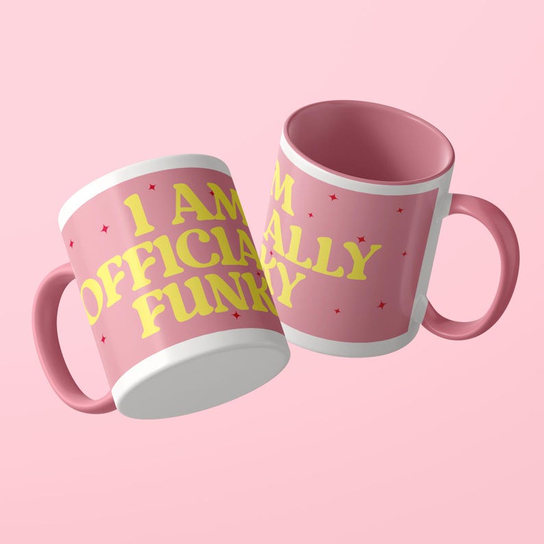May include: Two pink ceramic mugs with a handle on each. The mugs feature the yellow text I AM OFFICIALLY FUNKY printed in a bold, rounded font. Small red four-pointed star icons are scattered across the pink surface of both mugs.