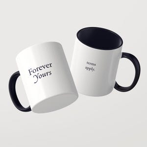 May include: Two white ceramic mugs with black interiors and black handles. One mug features the black text Forever Yours, while the other mug displays the black text terms apply. The mugs are positioned at an angle against a plain background.