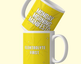 May include: Two white ceramic mugs with yellow exterior panels. The top mug features the black text MONDAY MORNING MANIFESTO with radiating lines. The bottom mug features the white text ELEKTROLYTE FIRST with radiating lines and small star icons.