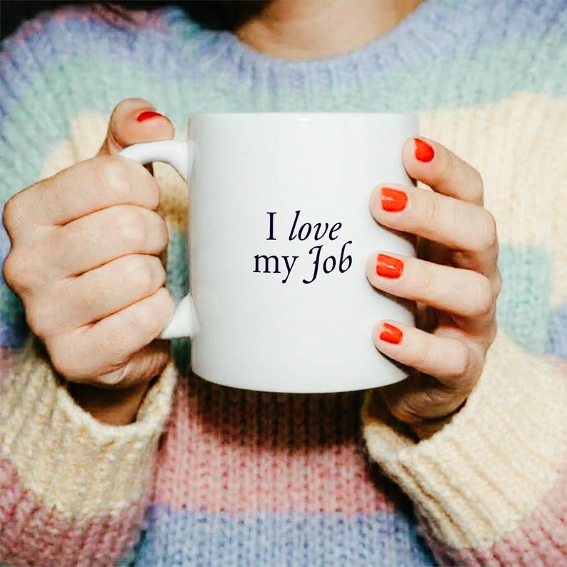May include: A white ceramic mug featuring the black text "I love my Job" printed in a serif font on the front. The mug has a smooth, cylindrical body and a curved handle on the side, designed for holding hot beverages in a standard capacity.