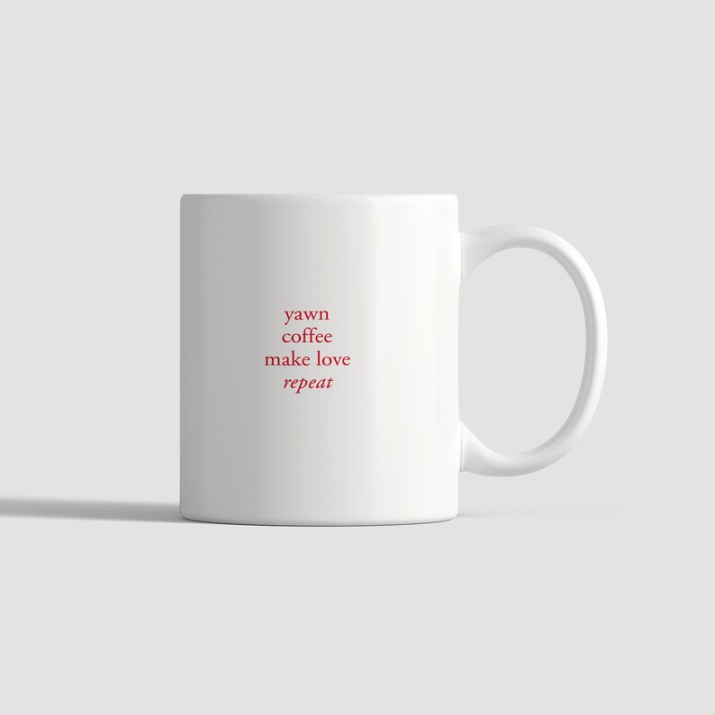 以下が含まれることがあります： 前面に「yawn coffee make love repeat」という赤い文字が中央揃えで積み重ねてプリントされた白いセラミック製のマグカップ。マグカップは滑らかな円筒形の本体と、右側から伸びる湾曲したハンドルを備えています。