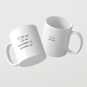 May include: Two white ceramic mugs featuring black printed text. One mug displays the French phrase C'est &ccedil;a &Ccedil;a va Comme ci, comme &ccedil;a, while the other mug features the phrase Je ne sais pas. Both mugs have a standard handle and cylindrical shape.