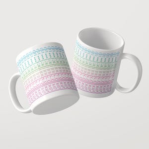 Puede incluir: Dos tazas de cer&aacute;mica blanca con un patr&oacute;n horizontal repetitivo de la palabra sunshine en un degradado de colores, que va del azul en la parte superior al verde, rosa y morado en la parte inferior, con peque&ntilde;os iconos de estrellas.