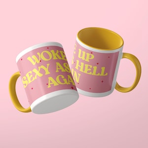 Może przedstawiać: Dwa ceramiczne kubki z ż&oacute;łtymi uszkami i wnętrzami. Zewnętrzna strona jest r&oacute;żowa z ż&oacute;łtym napisem WOKE UP SEXY AS HELL AGAIN oraz małymi czerwonymi gwiazdkami. Kubki są ustawione pod kątem, aby w pełni wyeksponować nadrukowany tekst.