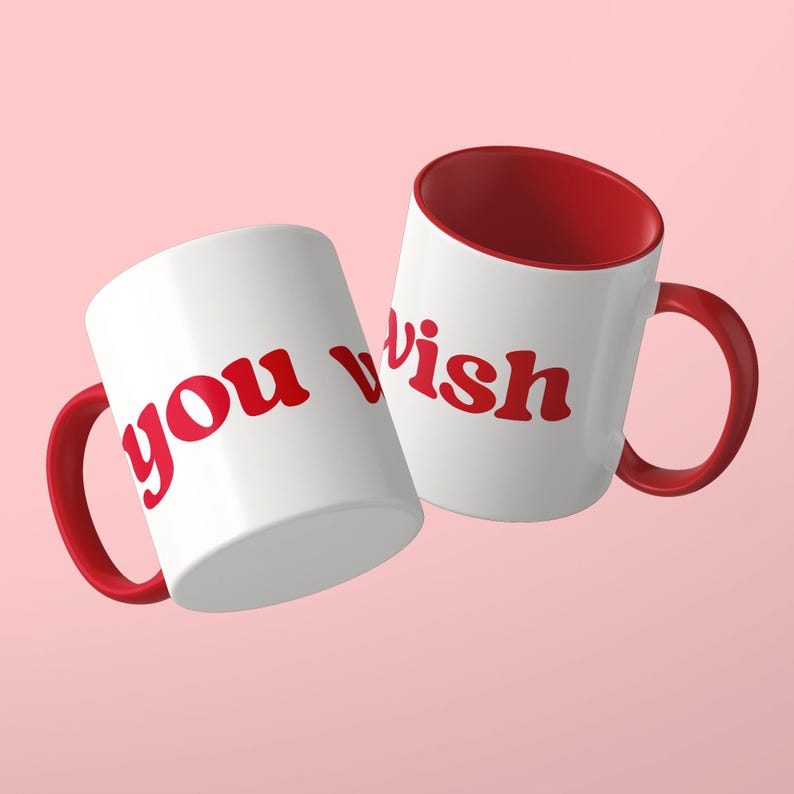 May include: Two white ceramic mugs with red interiors and red handles. The mugs feature the red text "you wish" in a bold, rounded font. The mugs are positioned at an angle, displaying the text clearly against the white exterior surface.