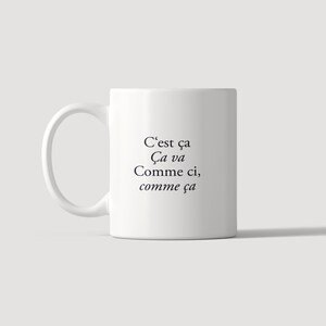 May include: A white ceramic mug with a handle on the left side. The front of the mug features black printed text that reads: C'est &ccedil;a, &Ccedil;a va, Comme ci, comme &ccedil;a. The mug has a smooth, cylindrical body and a clean, simple design.