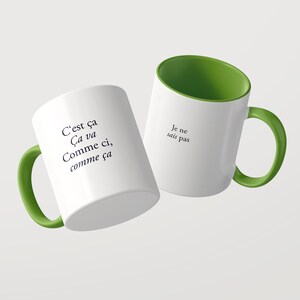 May include: Two white ceramic mugs with green interiors and handles. One mug features the black text C'est &ccedil;a &Ccedil;a va Comme ci, comme &ccedil;a. The other mug displays the black text Je ne sais pas. Both mugs have a smooth finish and a cylindrical shape.