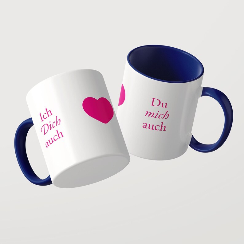 Pu&ograve; includere: Due tazze in ceramica bianca con interni e manici blu scuro. Le tazze presentano un testo color magenta che recita Ich Dich auch e Du mich auch, accompagnato da un grafico a forma di cuore magenta stampato sulla superficie esterna bianca.