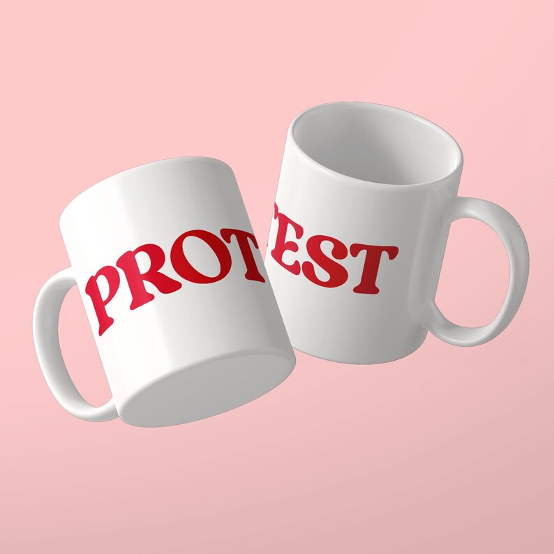 May include: Two white ceramic mugs featuring red lettering. The left mug displays the text PROT and the right mug displays the text EST in a bold, serif font. Both mugs have a standard handle and a smooth, glossy finish against a light pink background.