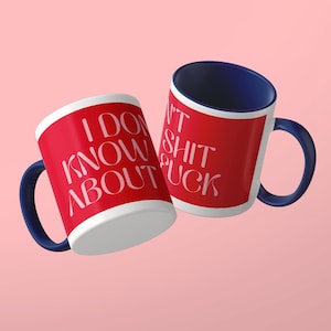 May include: Two ceramic mugs with a red exterior and a dark blue interior and handle. The mugs feature white text that reads I DON'T KNOW ABOUT SHIT FUCK in a stylized font. The mugs are positioned at an angle against a solid light pink background.
