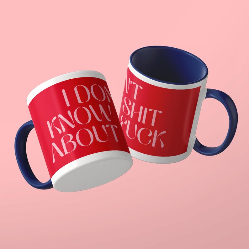 May include: Two ceramic mugs with a red exterior and a dark blue interior and handle. The mugs feature white text that reads I DON'T KNOW ABOUT SHIT FUCK in a stylized font. The mugs are positioned at an angle against a solid light pink background.